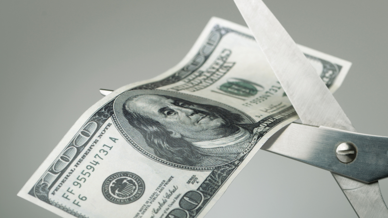 Scissors cutting a dollar bill in half. Image Credit: Adobe Stock Images/pogonici