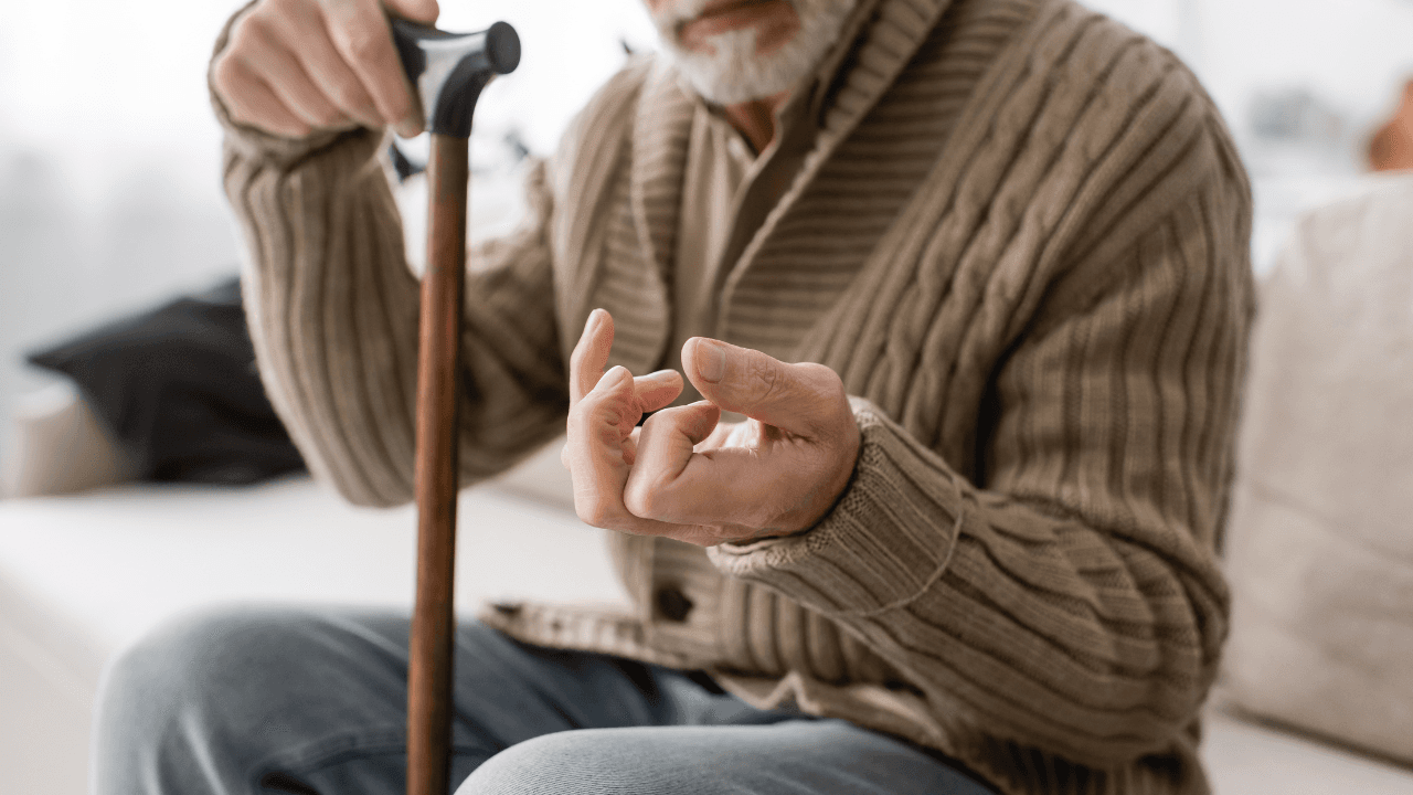 cropped view of senior man with parkinson disease holding walking cane while sitting on couch at home. Image Credit: Adobe Stock Images/LIGHTFIELD STUDIOS